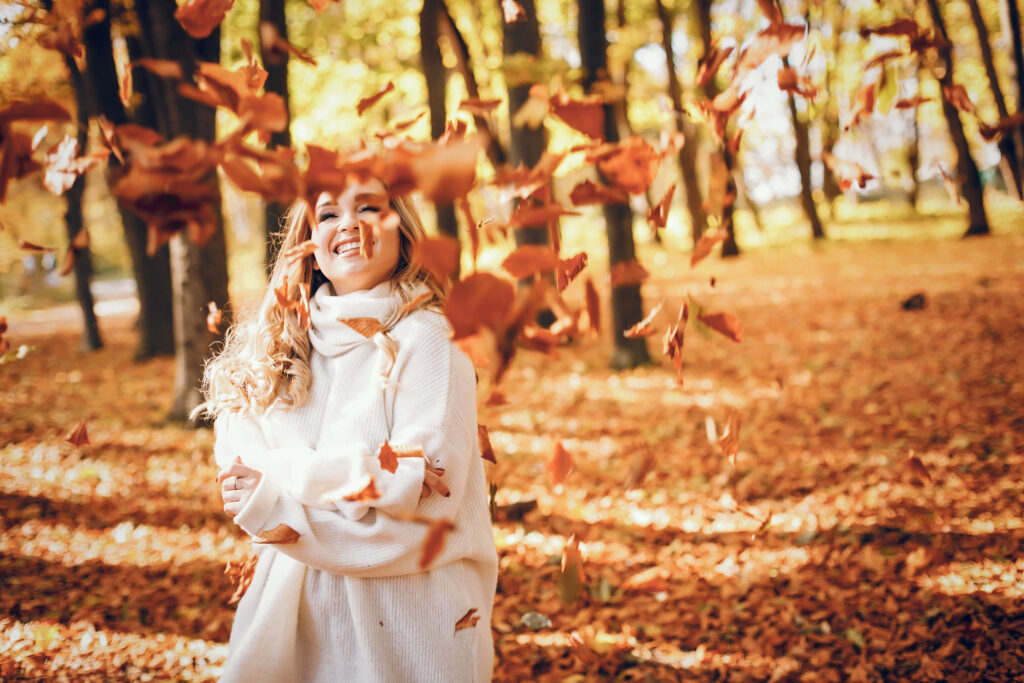 kobieta w parku jest szczęśliwa pośród jesiennych liści, bo wie jak pielęgnować skórę twarzy w okresie jesienno-zimowym